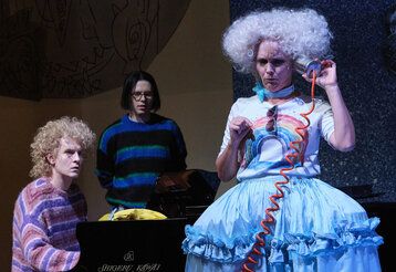 Szene aus der Oper Holle!, Frau Holle telefoniert mit einer Blechdose, zwei Personen gucken zu