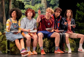 Fünf Jugendliche sitzen auf einer Theaterbühne vor einer Waldkulisse