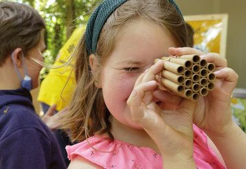 Mädchen im pinken Kleid guckt durch kleine Röhrchen, die zum eines Insektenhotels gebraucht werden