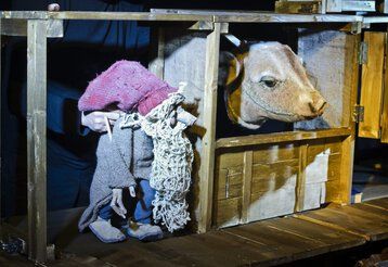 Ein Puppenspieler steht hinter einer Holzkulisse und spielt mit einer Wichtel- und einer Kuhhandpuppe