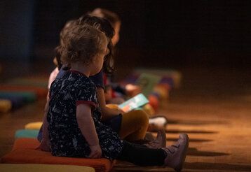 Kleine Mädchen sitzen in der Tonhalle auf Sitzkissen und lauschen einem Konzert