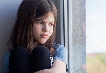 ein trauriges Mädchen sitzt am Fenster