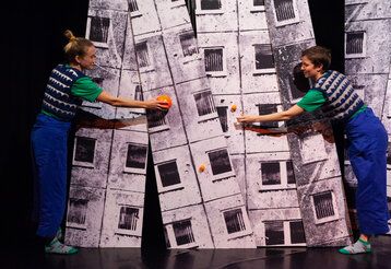 Zwei Schauspielerinnen spielen auf der Bühne mit orangen Kugeln