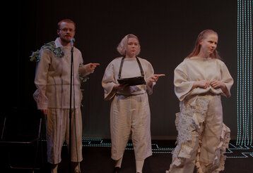 zwei Schauspielerinnen und ein Schauspielet stehen auf einer dunklen Bühne