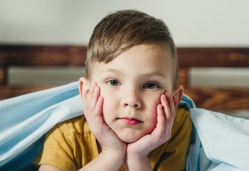 Junge liegt im Bett und guckt nicht fröhlich