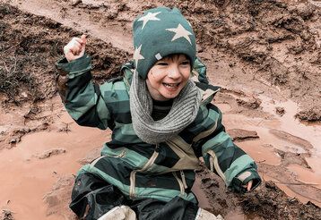 Ein Junge sitzt glücklich in einer Matsch-Pfütze