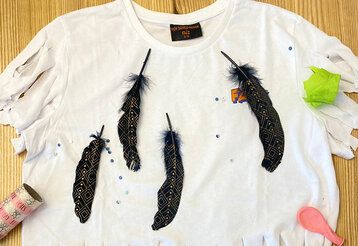 Ein weißes T-Shirt mit fransig geschnittenen Ärmeln und beklebt mit Federn und Glitzersteinchen