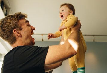 Vater hält Baby hoch und lacht