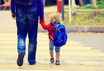 Vater und Kind überqueren Hand in Hand eine Straße, Sicht von hinten