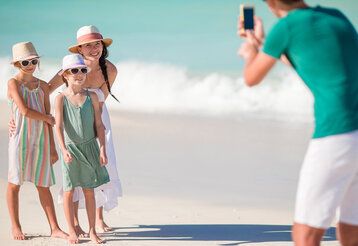Vater fotografiert seine Frau und zwei Töchter am Strand, im Hintergrund Brandung