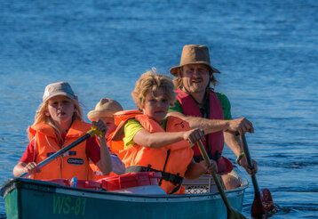 Vater paddelt mit Kindern im Paddelboot auf einem See