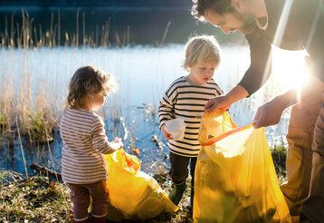 Vater sammelt mit seinen kleinen Kindern Müll im Freien