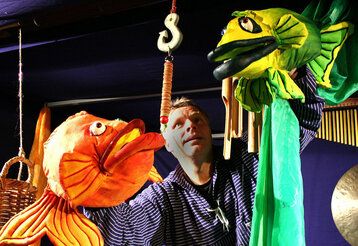 Puppenspieler mit zwei Fisch-Handpuppen in orange und grün