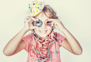 Kind hält sich zwei Luftschlangen vor die Augen