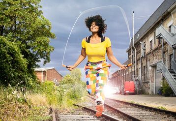Frau springt Seilchen auf Schienen in Industriegelände