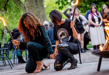 Zwei Frauen mit fackeln knien zusammen, im Hintergrund Publikum