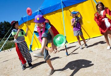 Verkleidete Kinder jonglieren mit Diabolos vor einem Zirkuszelt