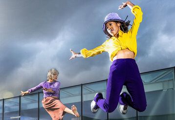 zwei Frauen tanzen und springen vor Wolkenhimmel