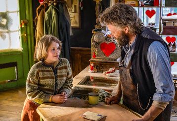 ein Kind steht bei einem Schuster am Verkaufstresen und spricht mit ihm