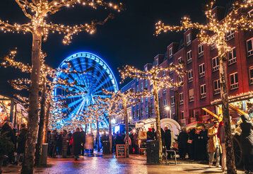 Weihnachtsmarkt-Stände auf der Rheinuferpromenade Düsseldorf am Abend, im Hintergrund das beleuchtete Riesenrad