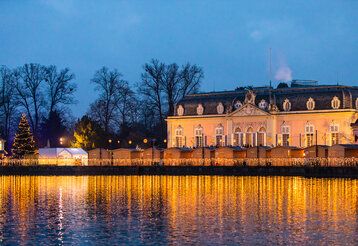 Weihnachtsmarkt vor dem Schloss Benrath am Abend, Lichterspiegelung im Wasser