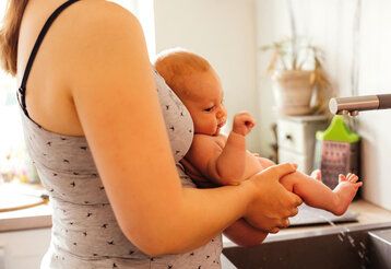 Eine Mutter hält ihr Baby über dem Waschbecken ab und das macht Pipi