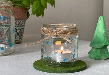 Zwei bemalte Konservengläser mit Teelichtern auf Tisch, daneben gebastelter Tannenbaum aus Eierkarton