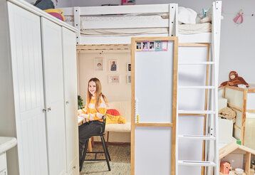 Kinderzimmer, Mädchen sitzt unter seinem Hochbett am Schreibtisch und lächelt in die Kamera