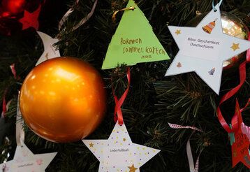 Detailansicht eines geschmückten Weihnachtsbaums mit Kugel und Papiersternen, auf denen Wünsche stehen