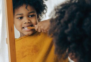 Kleiner Junge putzt sich die Zähne und betrachtet sich dabei im Spiegel