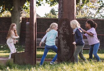 Vier Kinder haben Spaß während sie im freien um Stahlskulpturen laufen