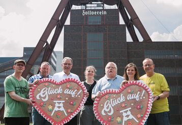 Sieben Leute stehen mit zwei großen Lebkuchenherzen vor der Zeche Zollverein