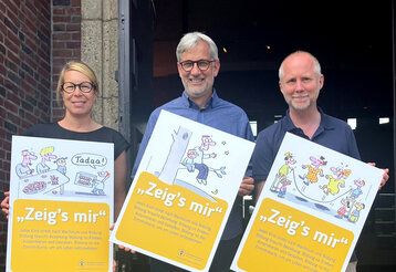 Eine Frau und zwei Männer stehen vor dem NRW Forum und zeigen Plakate des Kinderschutzbundes.