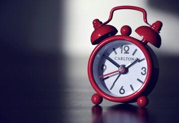 Kleiner roter Wecker im antiken Stil zeigt zehn Minuten vor zwei an