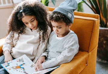 Zwei Kinder sitzen auf einem Sessel und lesen ein Buch