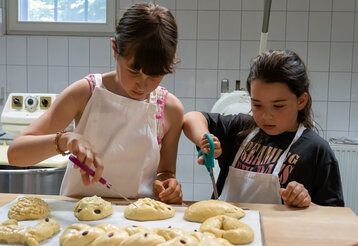 zwei Mädchen in der Backstube, vor ihnen liegen geformte, rohe Hefeteiggebilde