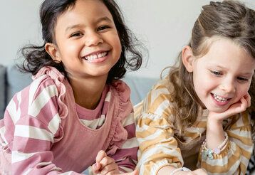 Zwei Mädchen sitzen nebeneinander und lachen