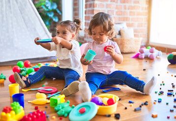 Zwei Mädchen sitzen auf dem Fußboden und spielen mit buntem Spielzeug