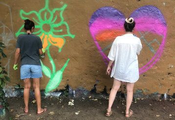 Zwei Mädchen sprühen Graffiti an eine Wand