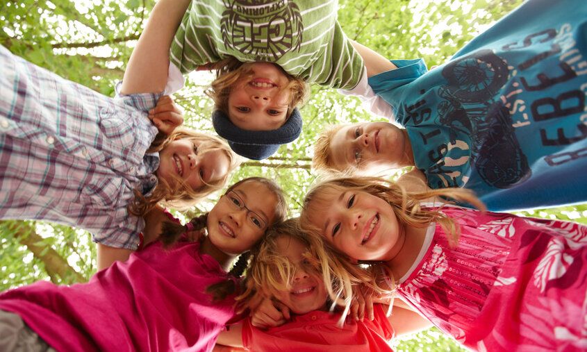 Sechs Kinder stehen im Kreis und umarmen sich, von unten fotografiert