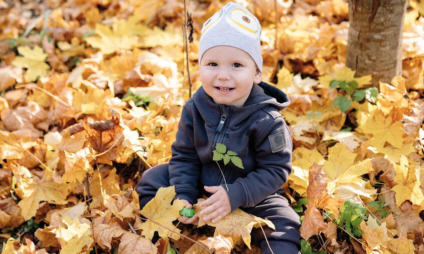 Lachendes Kleinkind mit Mütze sitzt im gelben Herbstlaub