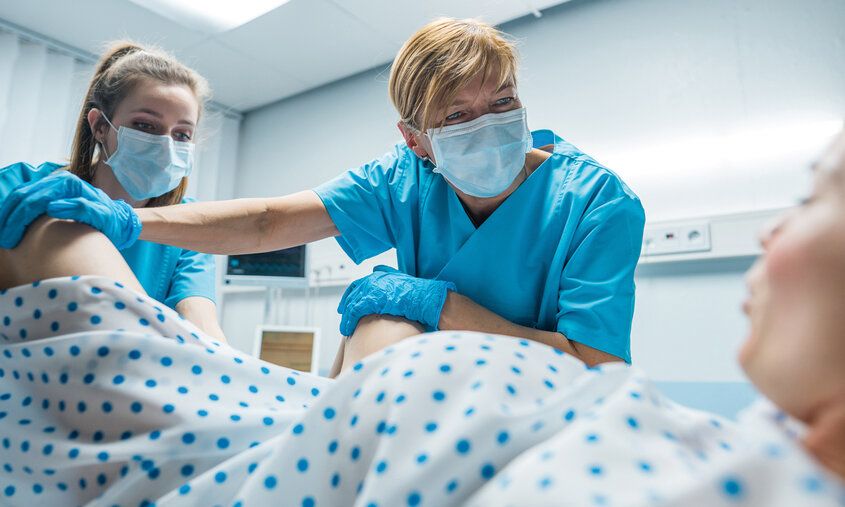Eine Frau wird bei der Geburt im Kreißsaal von zwei Hebammen betreut