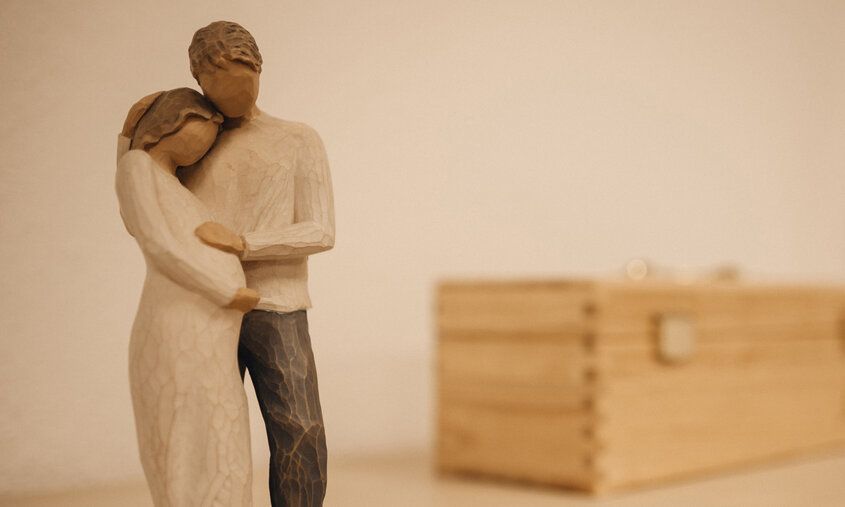 Holzfiguren, eine schwangere Frau und ein Mann, der sie umarmt und den Bauch streichelt