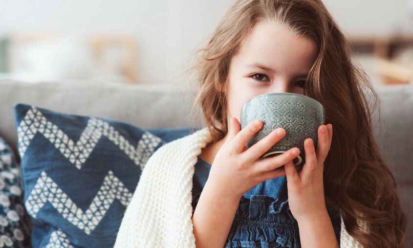 Mädchen sitzt auf einem Sofa und trinkt aus einer Tasse