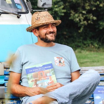 Autor Ben Walleborn sitzt mit einem Buch auf einer Parkbank 