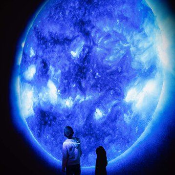 Zwei Menschen stehen vor dem Bild eines großen, blau leuchtenden Mondes