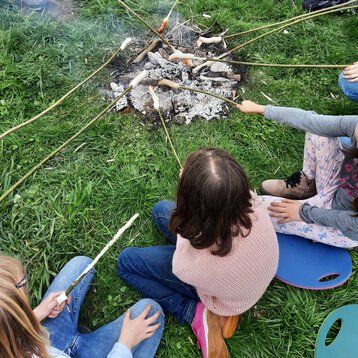 Kinder sitzen an einem Lagerfeuer und grillen Würstchen am Stock